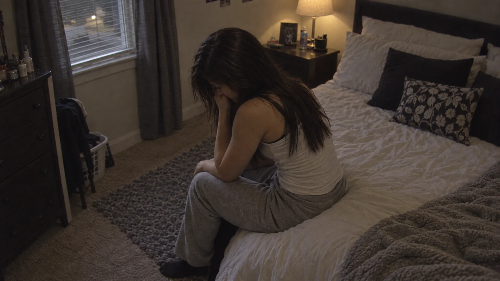 A distressed young woman sitting on the edge of a bed