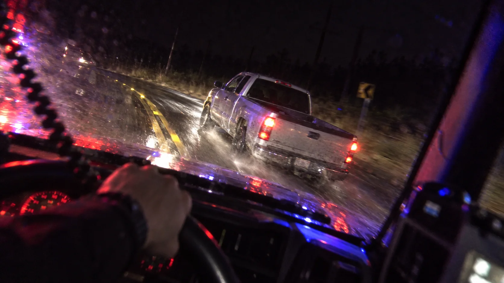 A police vehicle pursuing a truck on a rain-slicked road at night