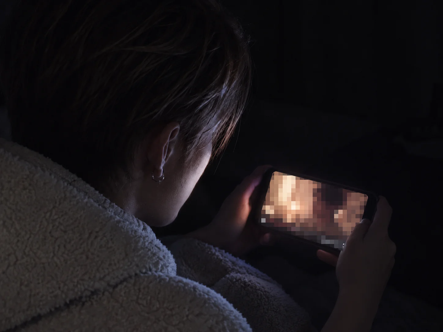 A person looking at a blurred private video on a phone in the dark