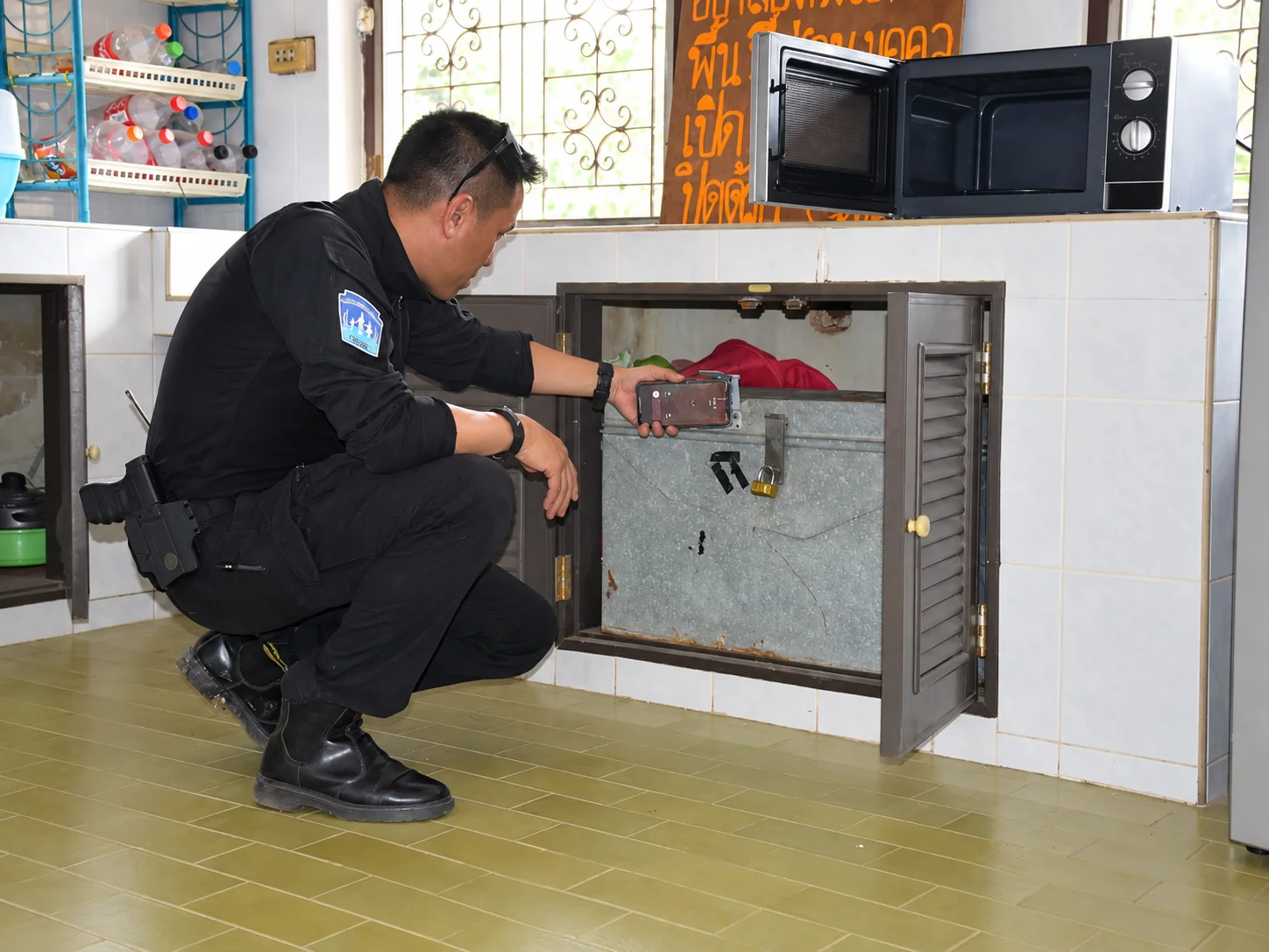 A police officer examining a locked metal box built into a cabinet