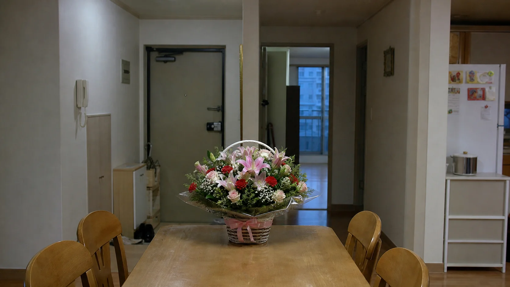 A basket of fresh flowers on a dining table in an apartment, with the front door behind it
