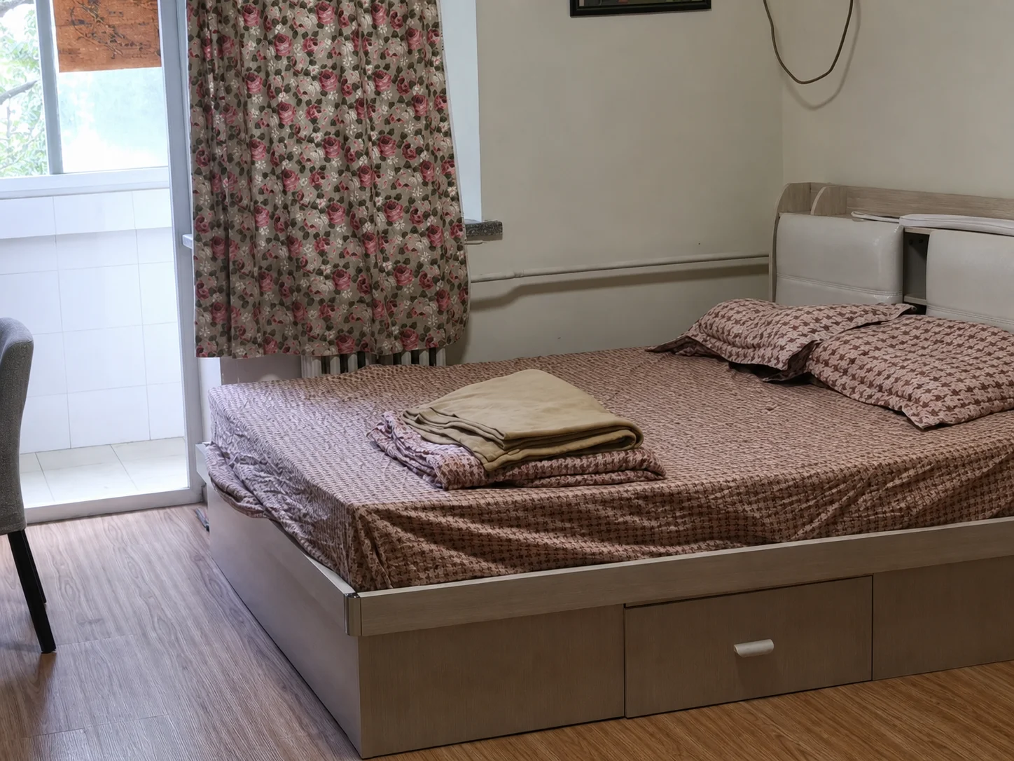 A double bed in a small bedroom with floral curtains