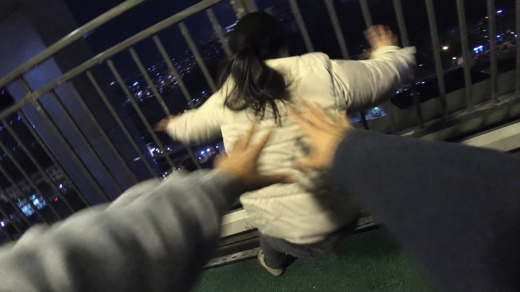 Two pairs of hands pushing a girl in a white jacket against a railing at night