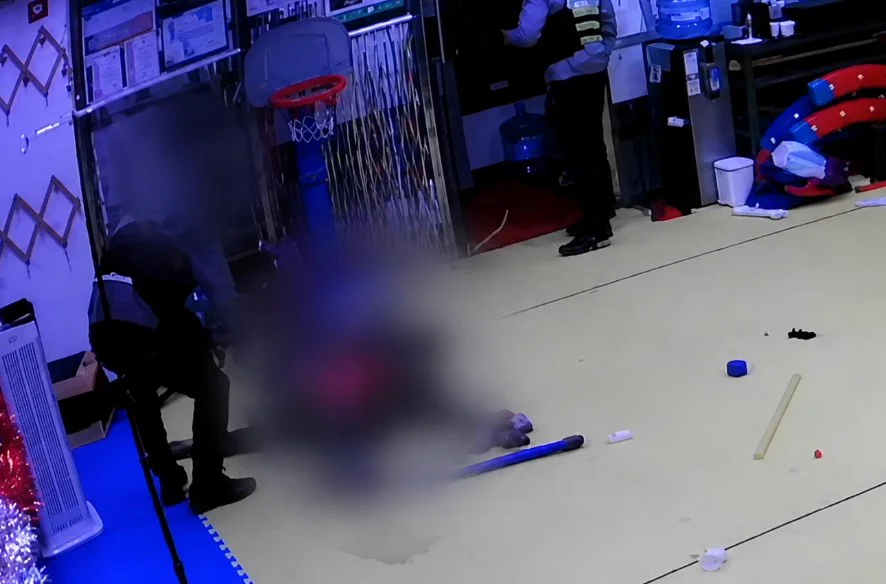 Security camera footage of police officers in the gym beside a blurred figure on the floor, with a blue rod lying nearby