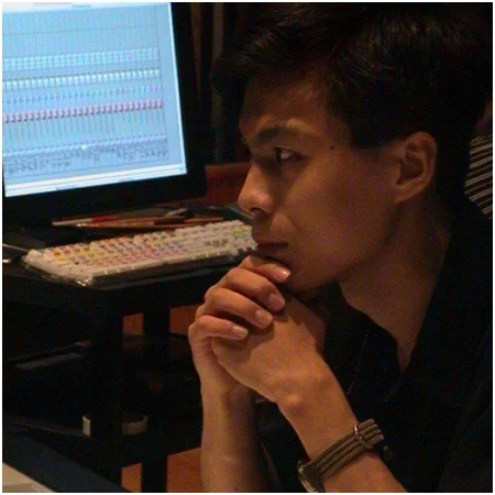 A man sitting at a studio workstation with his hands clasped in front of a monitor