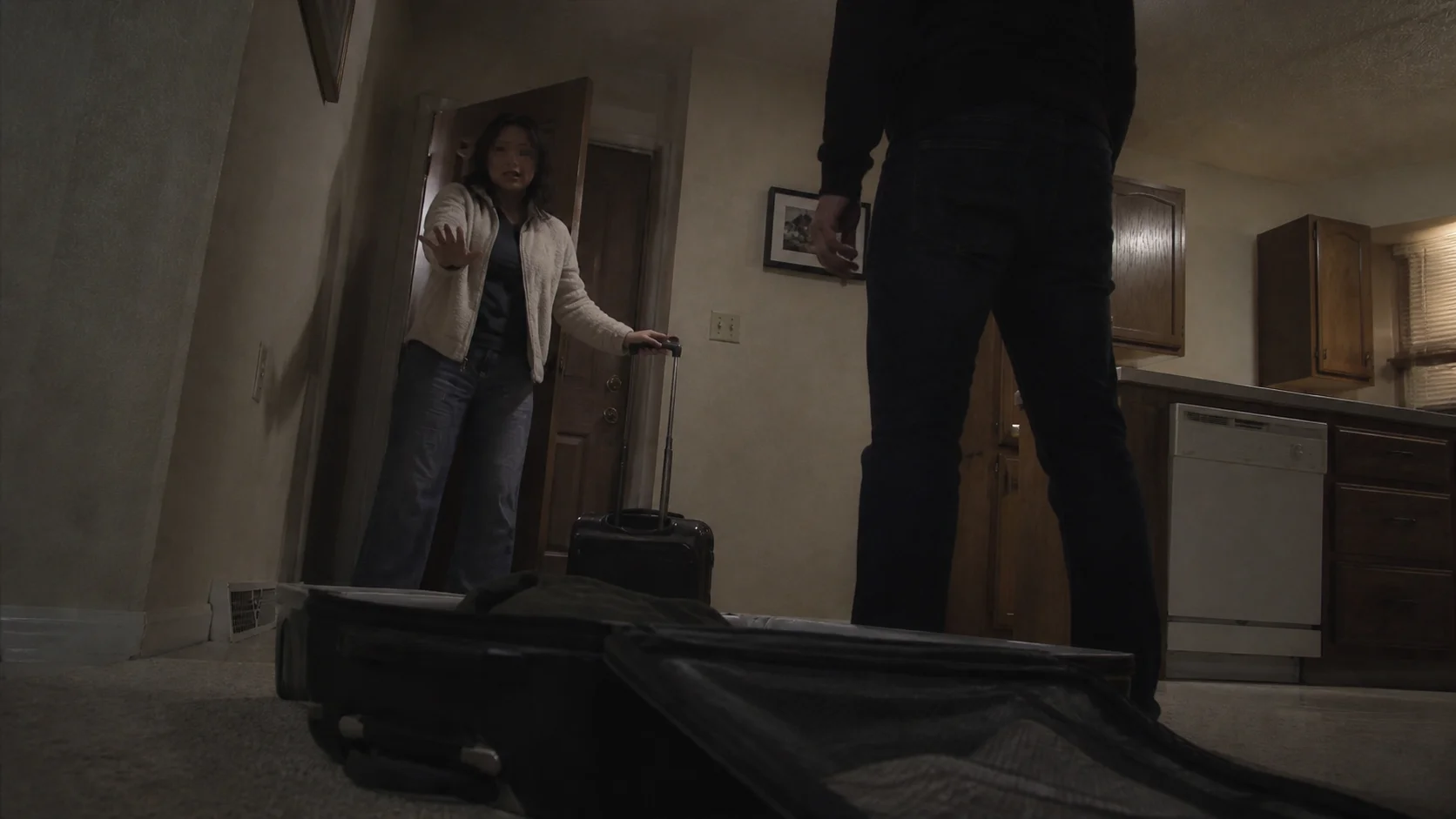 A woman with a suitcase raising her hand toward a man standing in front of her inside a house
