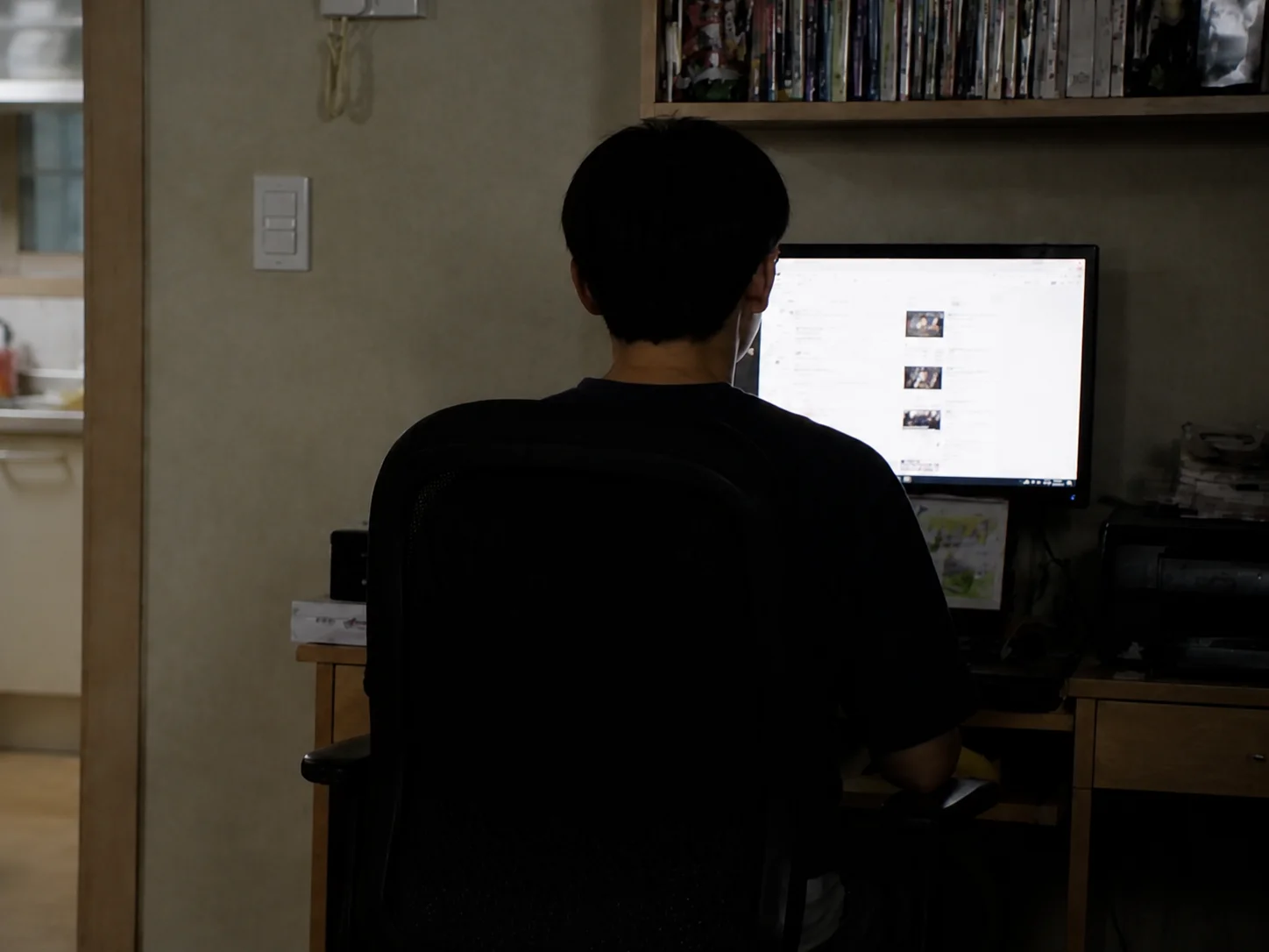 A person seen from behind sitting at a computer in a dimly lit room