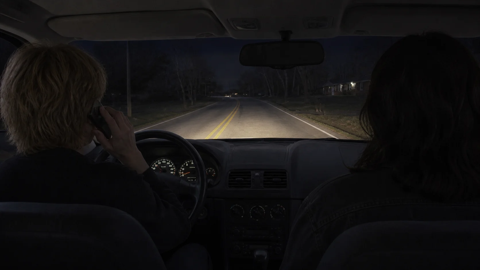 Two people in a car on a dark road at night, the driver holding a phone to her ear