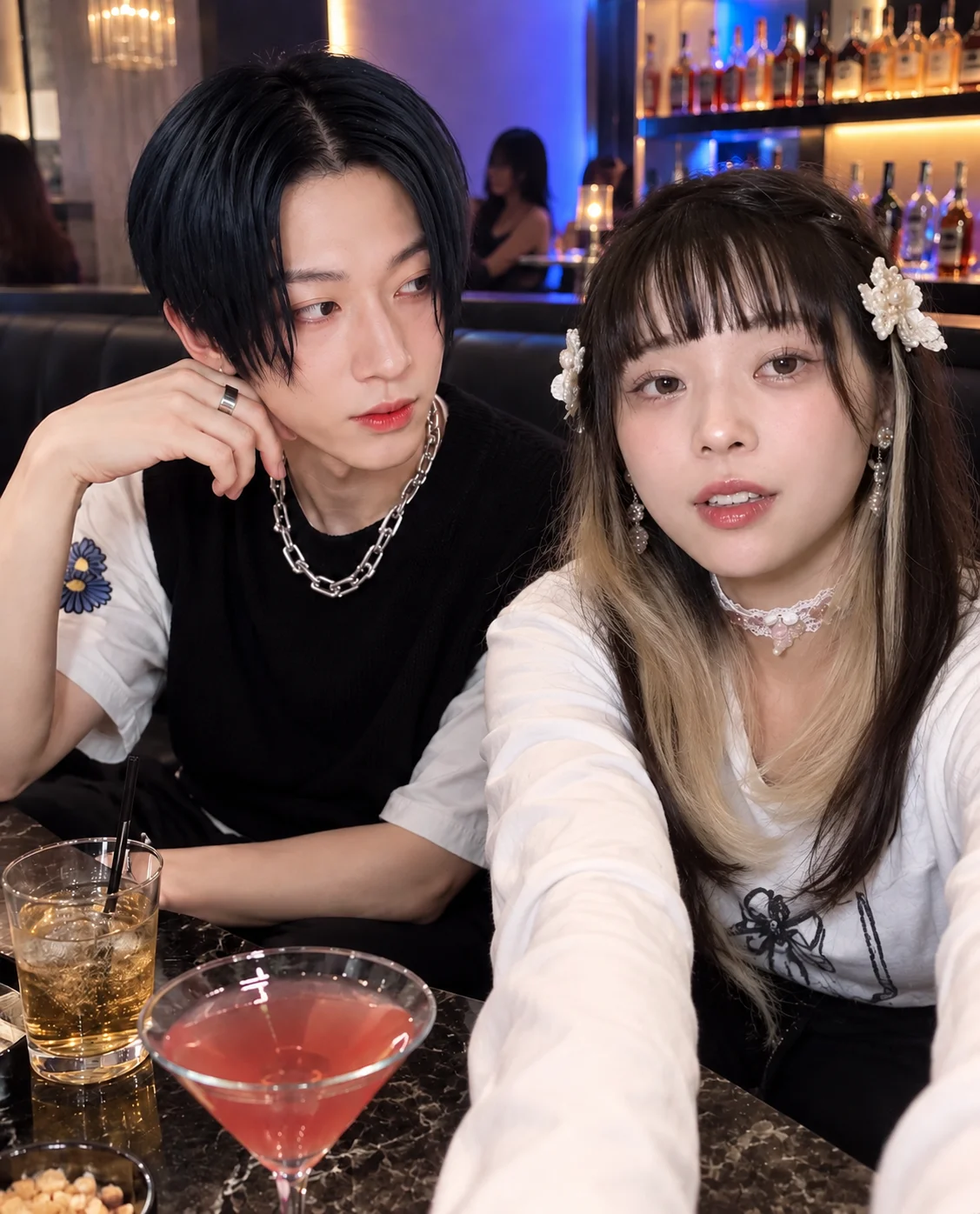 A young woman taking a selfie beside a young man in a dimly lit club, with drinks on the table and bottles lining the bar behind them