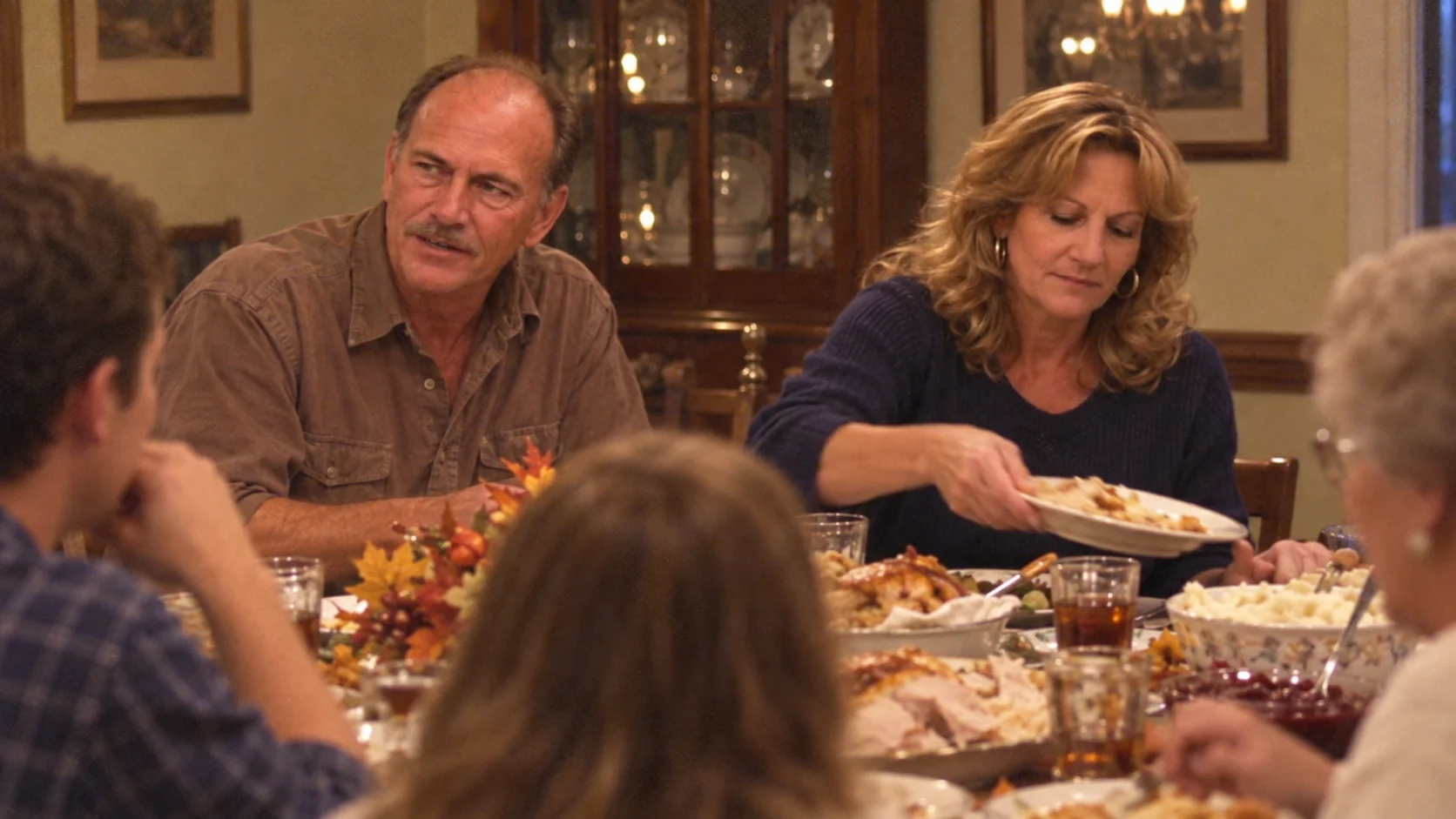 An older man and a woman seated at a crowded Thanksgiving dinner table with family members in the foreground