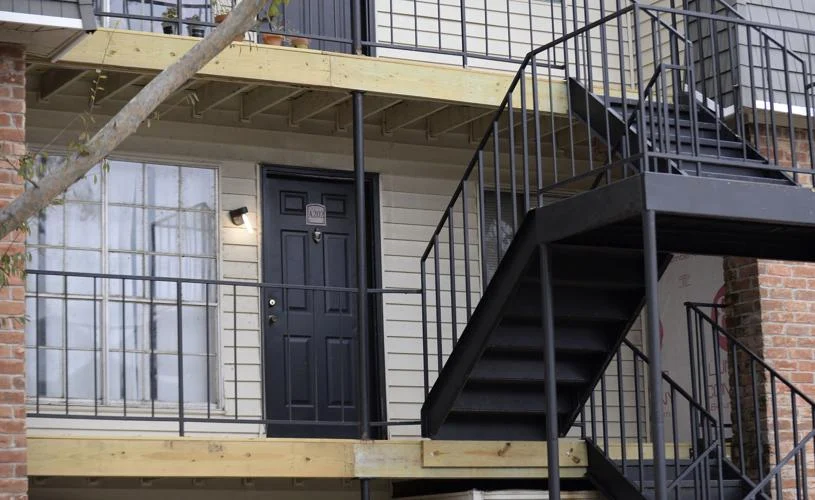 The black front door of a ground-floor apartment beneath an exterior metal staircase