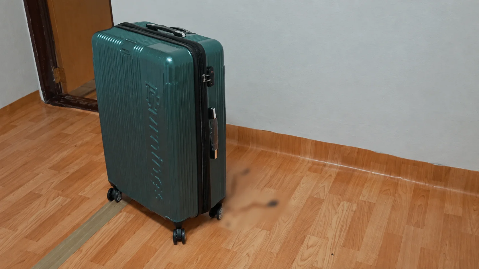 A large green hard-shell suitcase standing on a wooden floor in an empty room