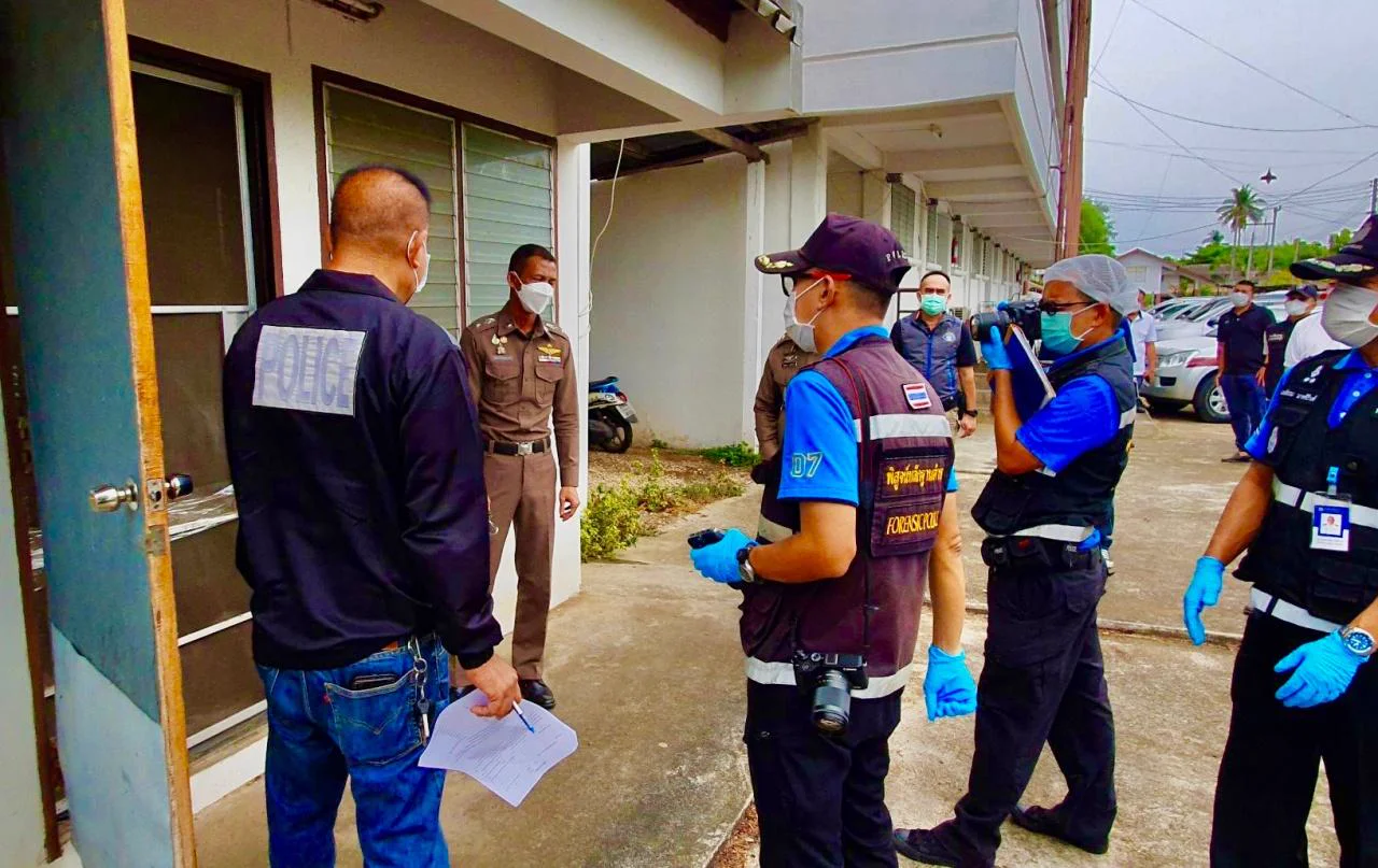 Thai police officers and forensic investigators with cameras and gloves gathered outside the open door of a building
