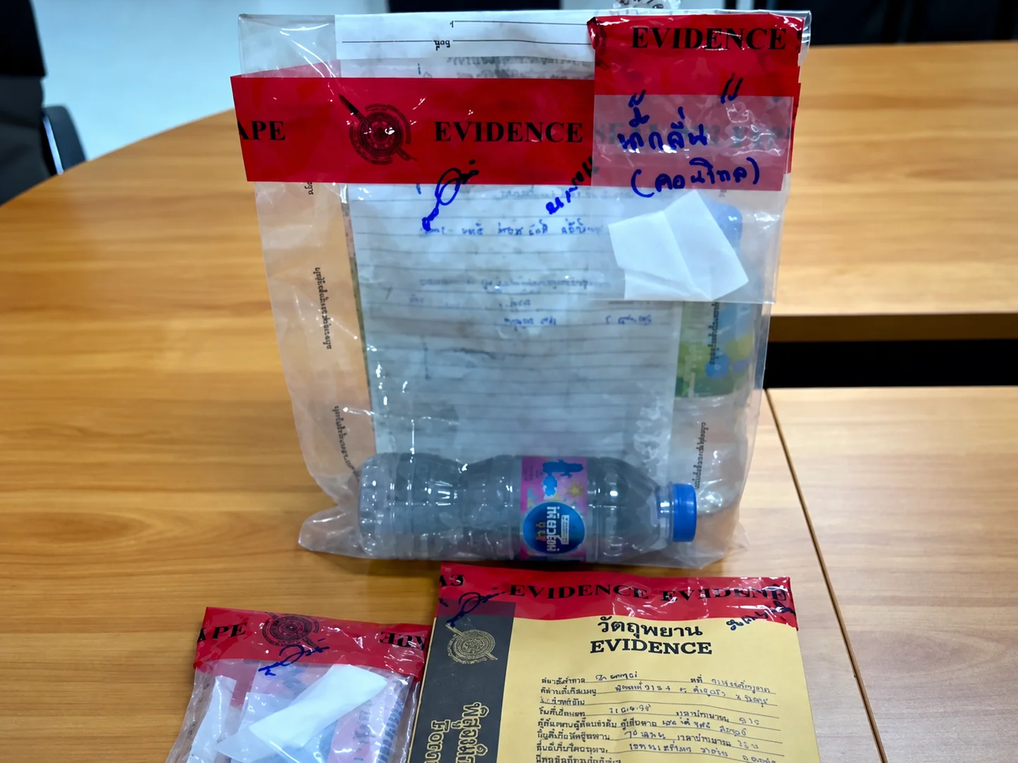 Sealed evidence bags with red evidence tape on a table, one holding an empty plastic water bottle and handwritten documents