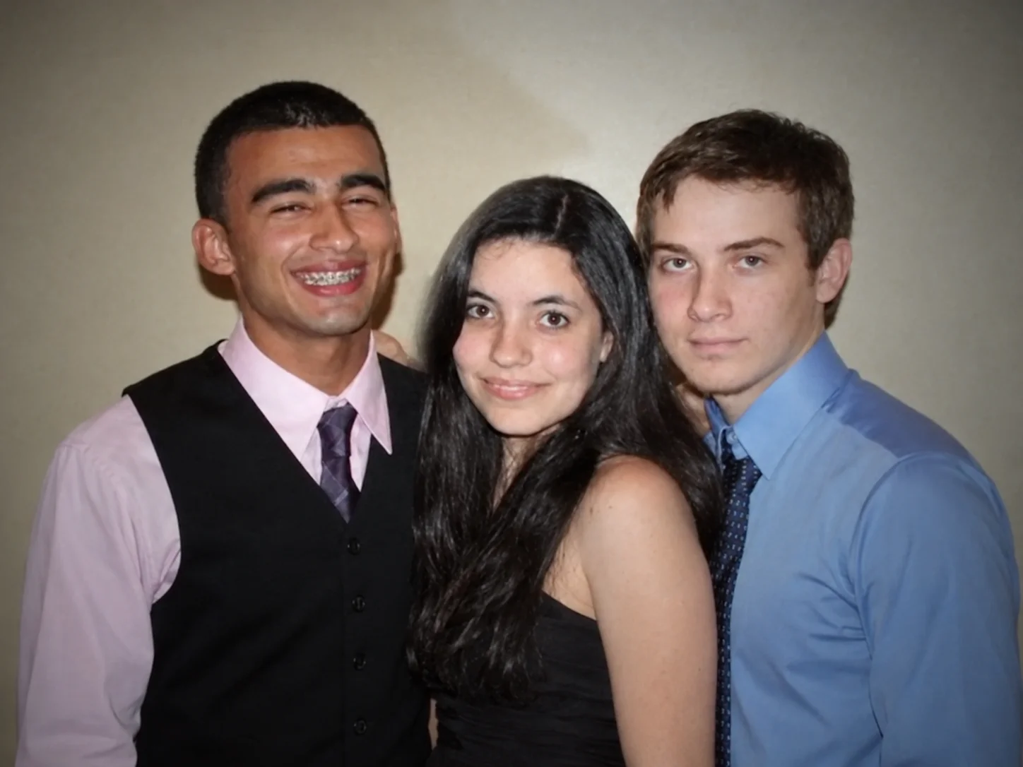 Two young men in dress shirts and ties posing with a young woman with long dark hair between them