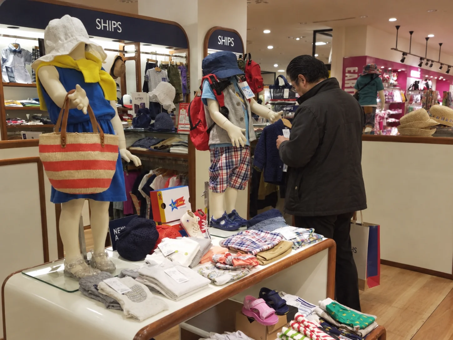 A middle-aged man browsing children's clothes at a shop with child mannequins