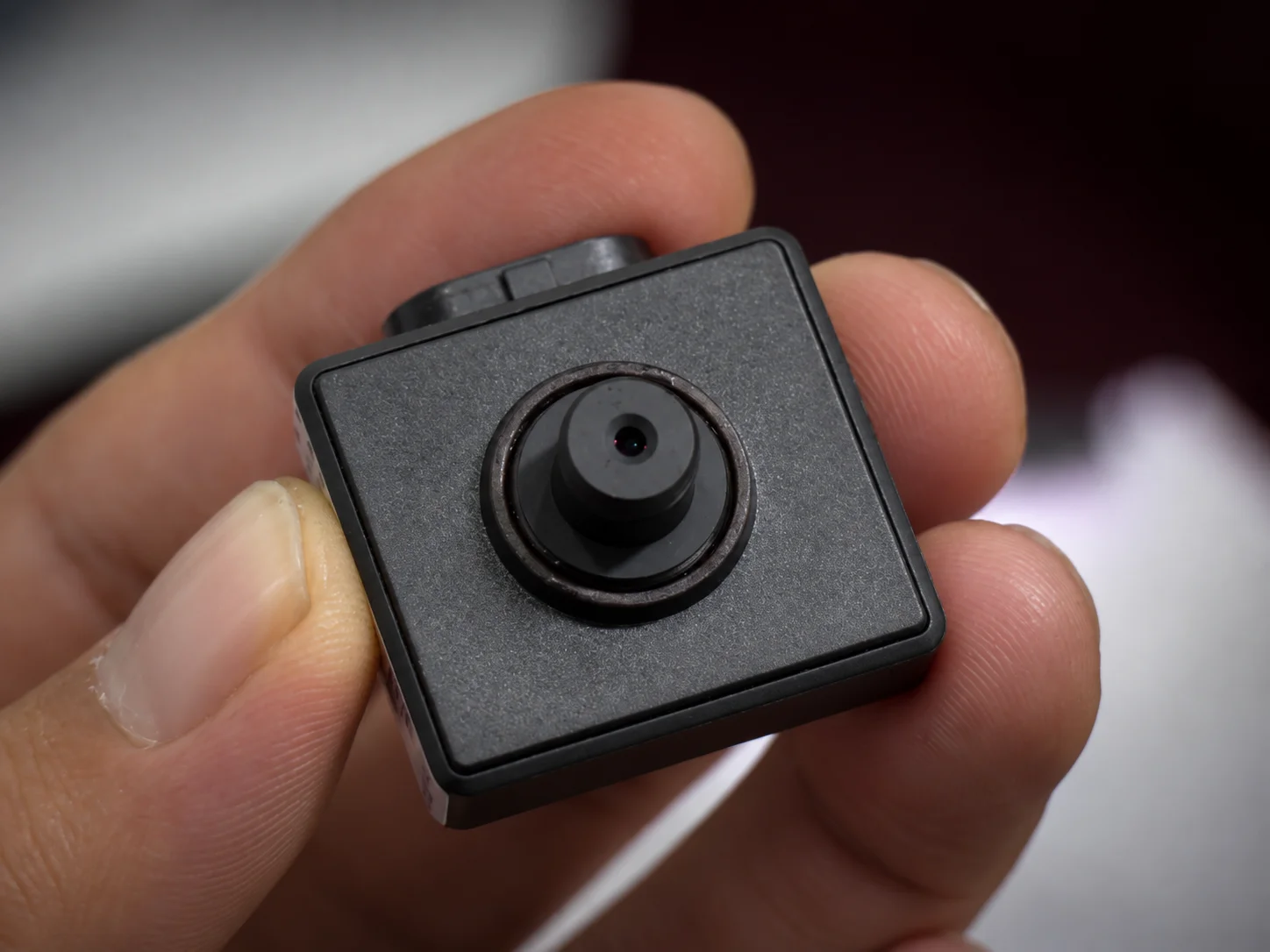 Fingers holding a tiny square pinhole camera