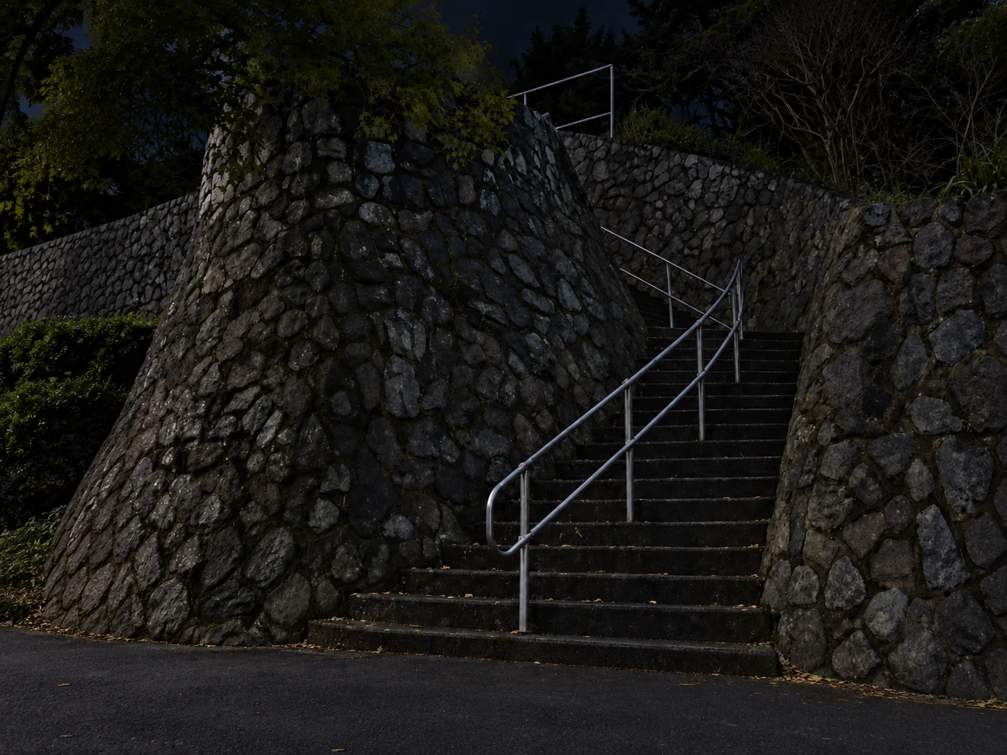 A flight of stone-walled park stairs with a metal handrail at night